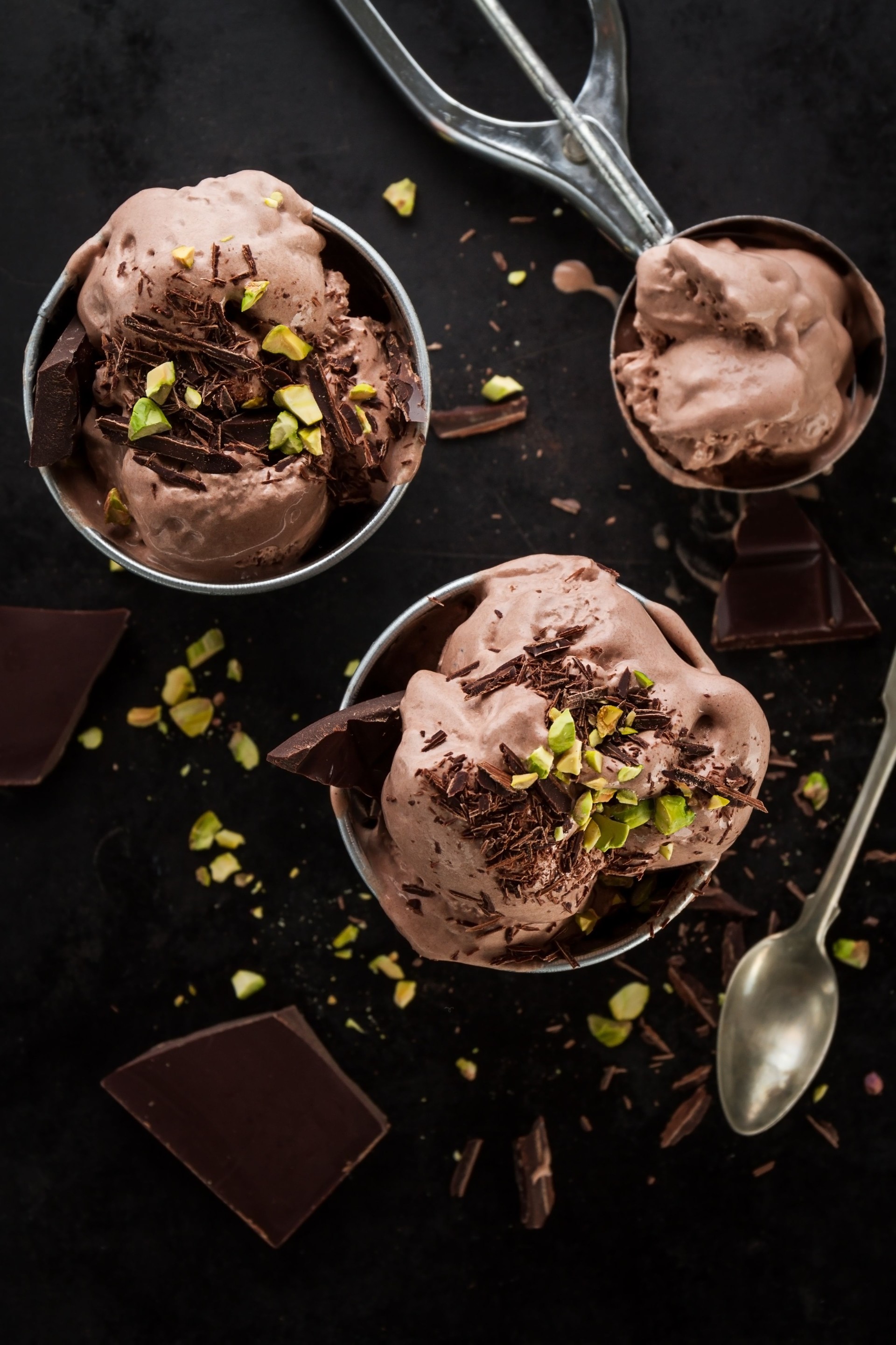Tasty appetizing chocolate ice cream with mint and pistachios in small cups on dark background. Cooking process. Top View.